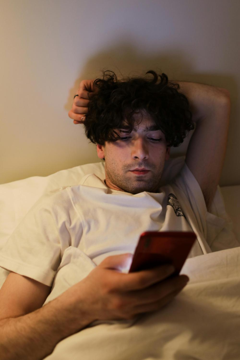  Man ligt op bed en pakt telefoon op.